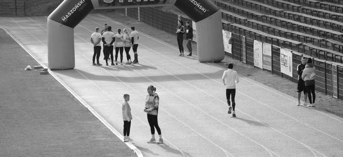 Black and white image of a running track with people near a start banner.