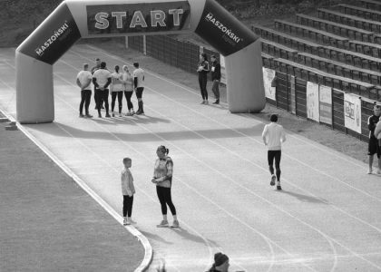 Black and white image of a running track with people near a start banner.